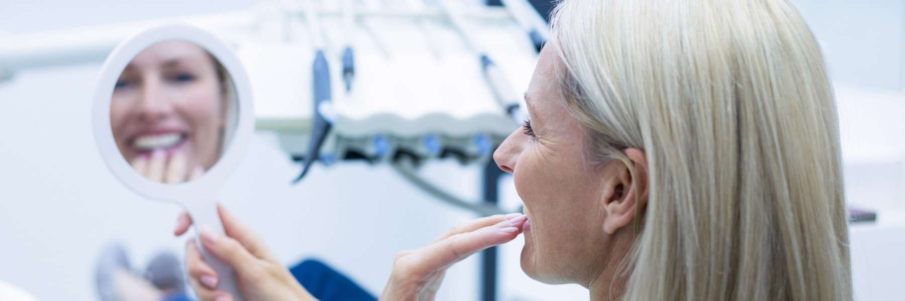 Older woman looking at teeth in mirror, brentwood tn